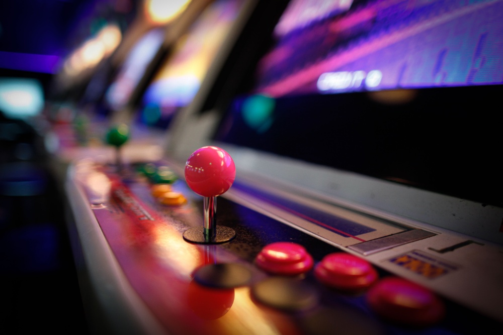 Close-up of an arcade joystick and illuminated buttons under neon light, representing arcade and console gaming